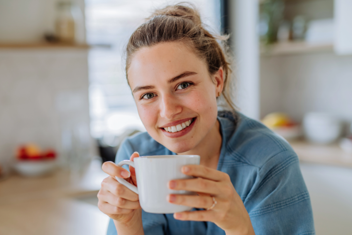 Junge Frau mit Dutt sitzt am Tisch und hält eine Tasse.