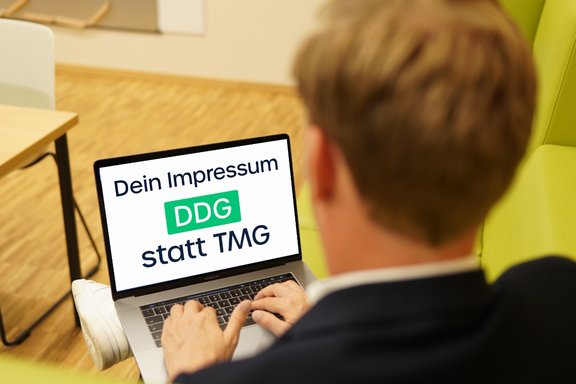 Blick schräg über die Schulter eines Mannes, der auf seinen Laptop schaut.